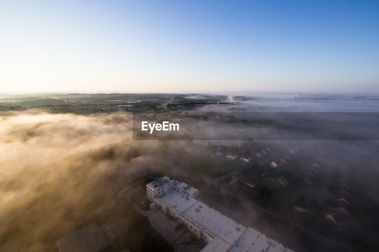 Aerial view of clouds covering town in clear sky