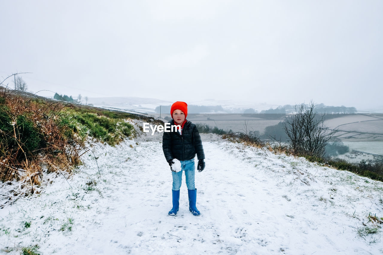 Portrait of cute boy standing on snow covered mountain road at winter