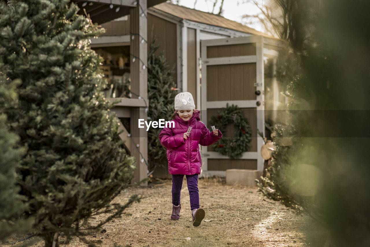 Cheerful girl holding candy canes walking by christmas trees at yard