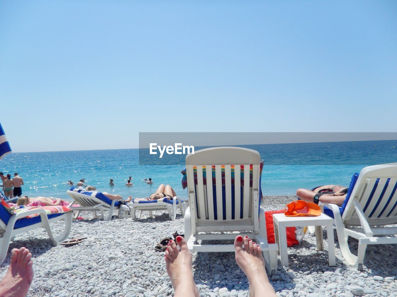 People relaxing on lounge chairs at beach against clear sky on sunny day