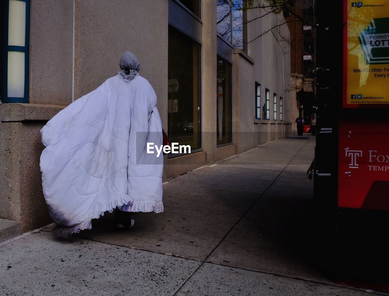 Rear view of woman in ghost costume walking on footpath during halloween