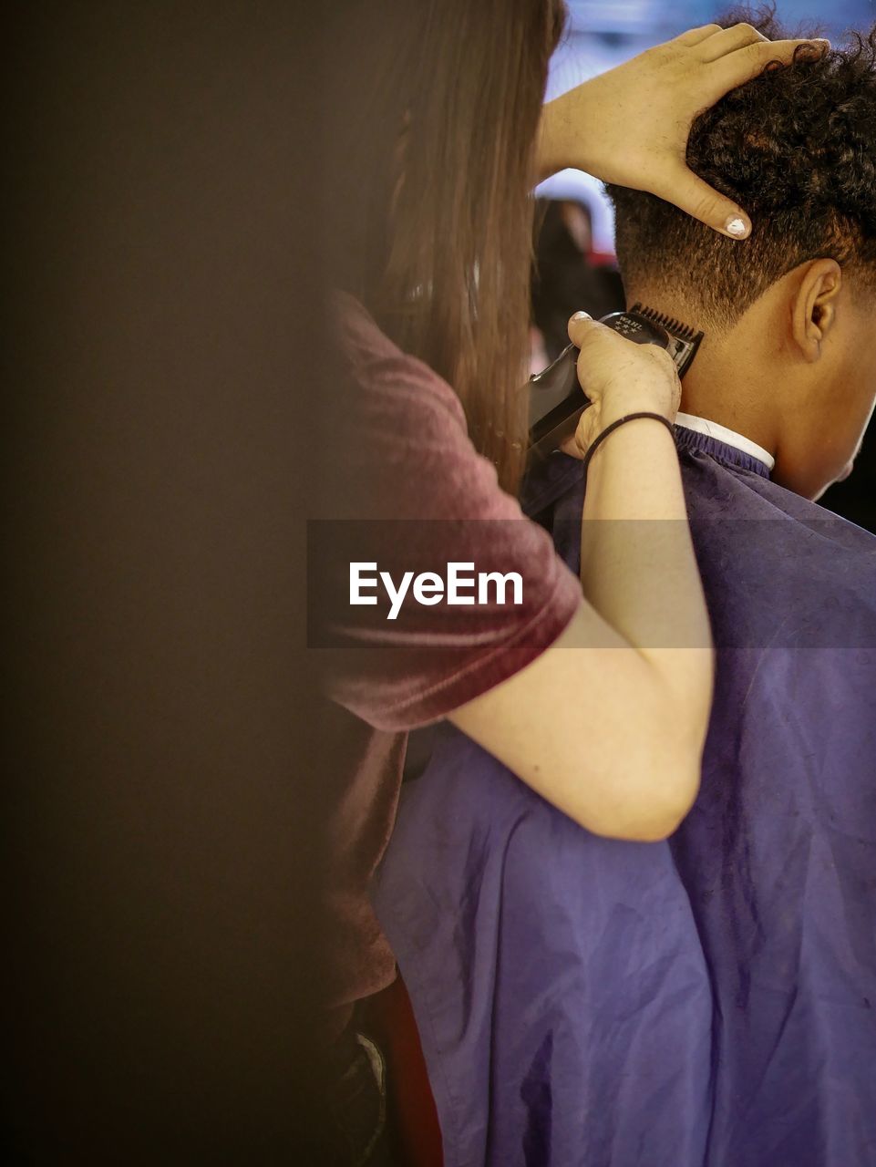 Woman shaving head of boy at barber shop