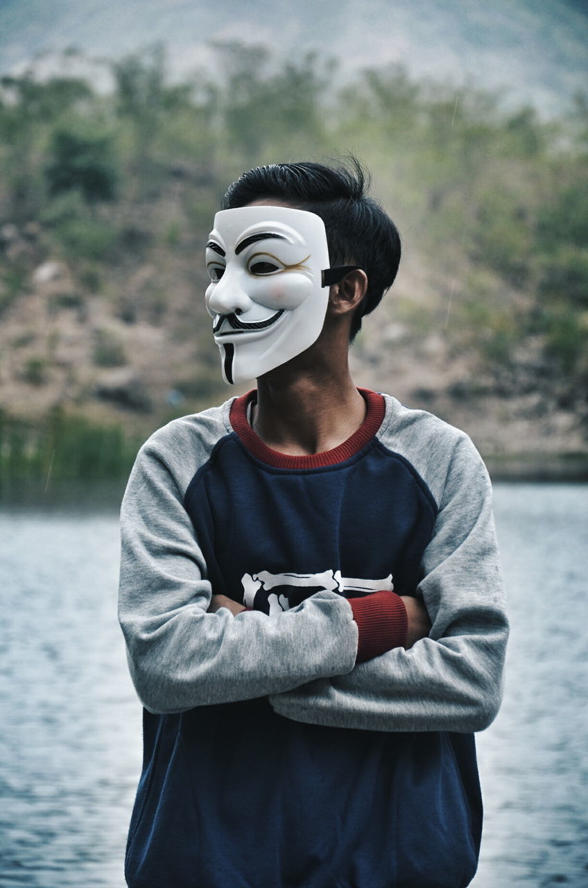 Man wearing mask while standing against lake