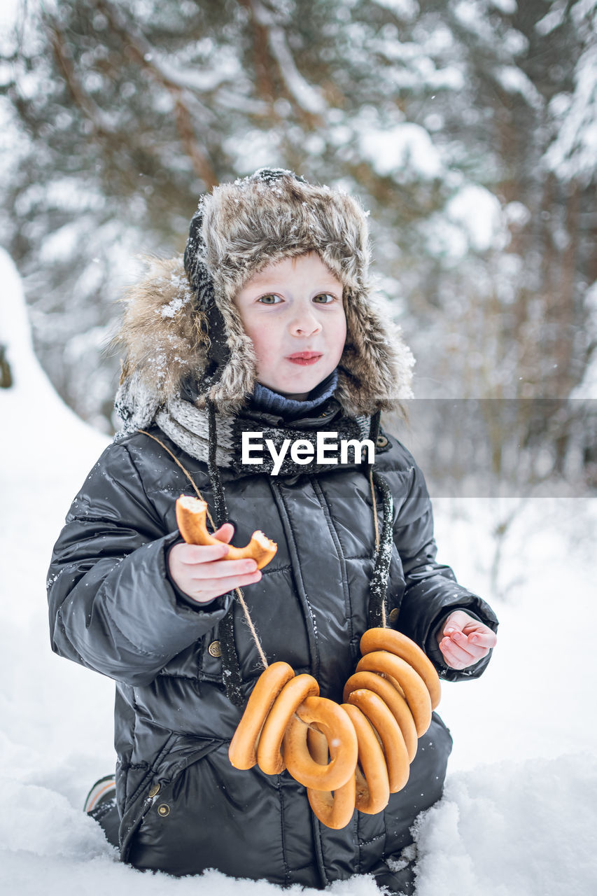 Russian boy with bagels around his neck and a string bag of tangerines outside in winter