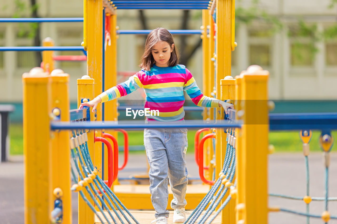 Little cute girl 5-6 years old on a childrens ladder on a bright yellow playground