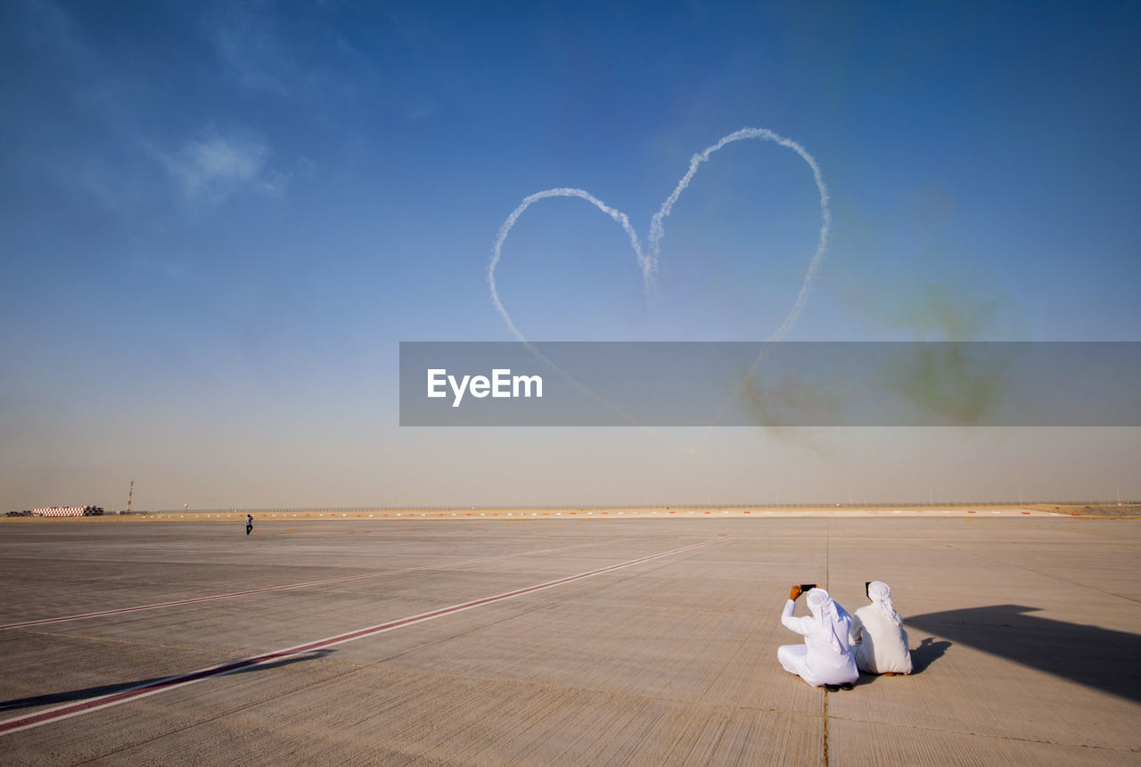 Men photographing heart shape contrail against sky