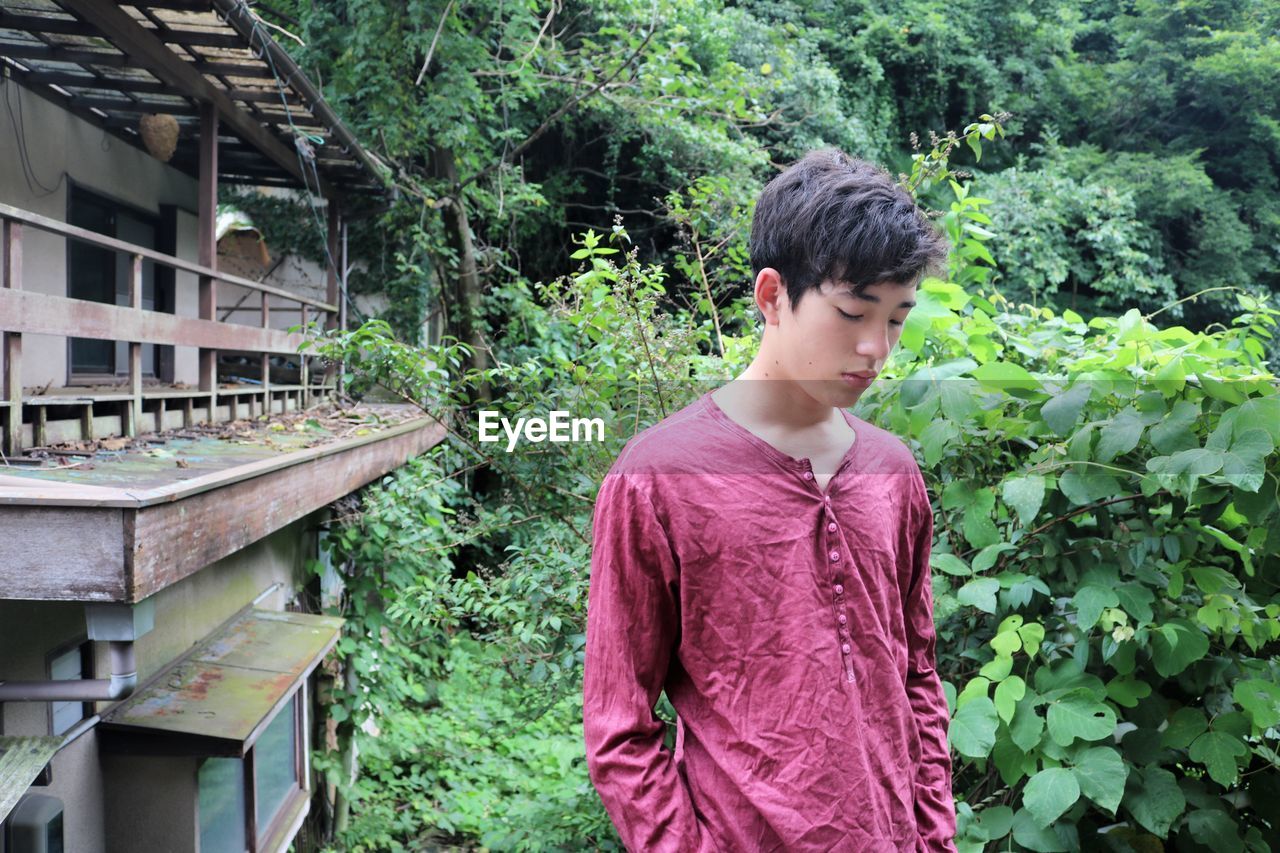 Side view of young man outside old house looking down