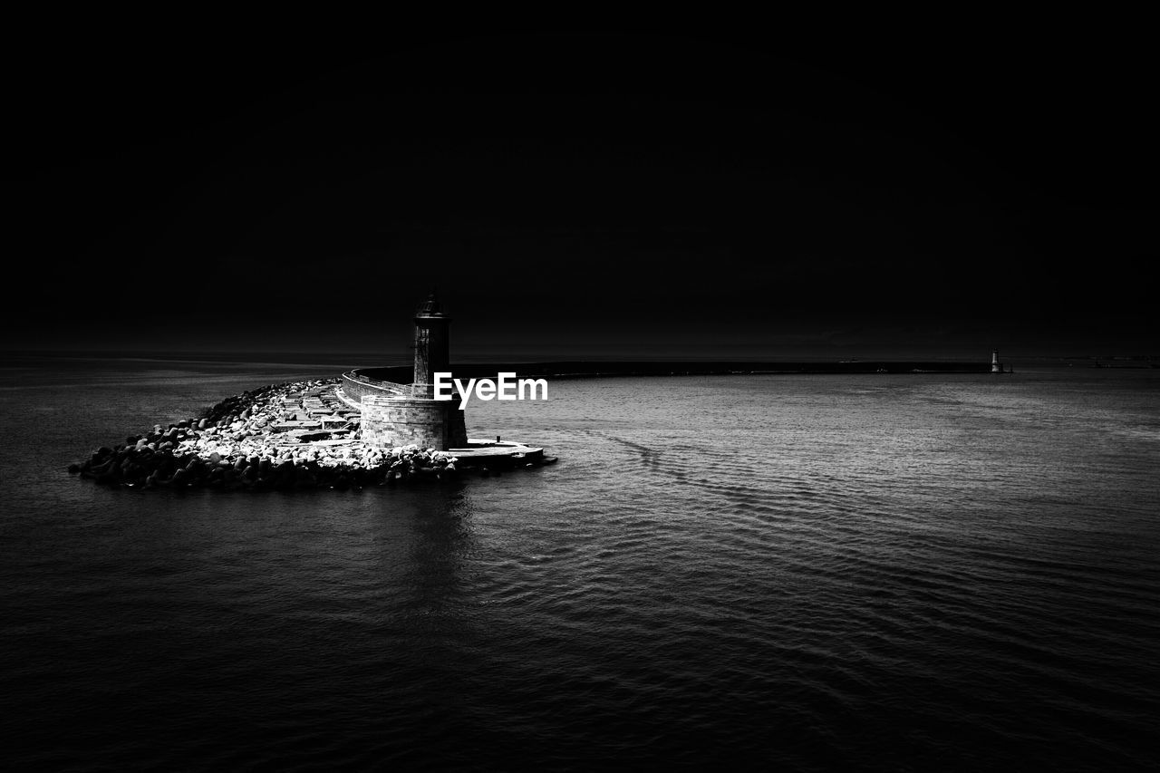 Lighthouse by sea against sky at night