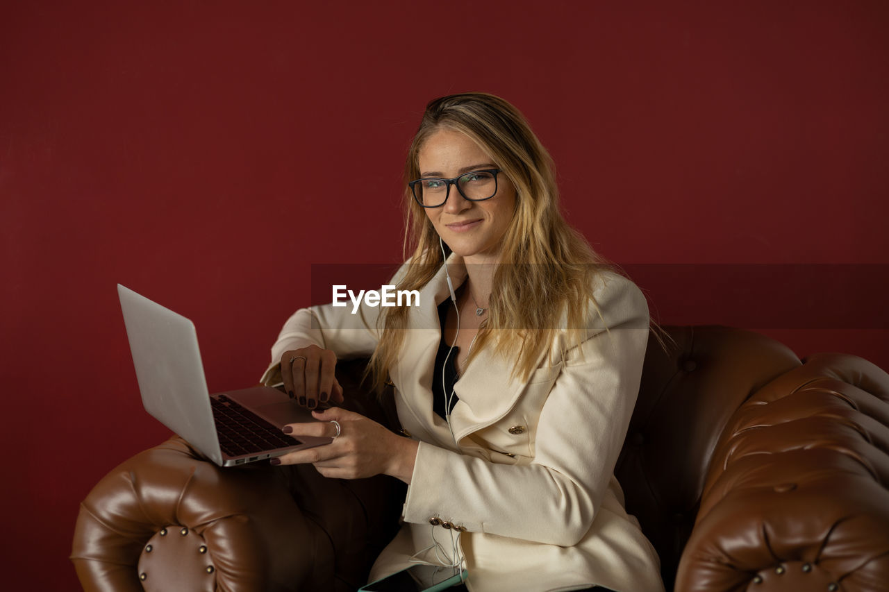 Woman working at home with laptop classic brown arm chair. red  wall home office. gray notebook 