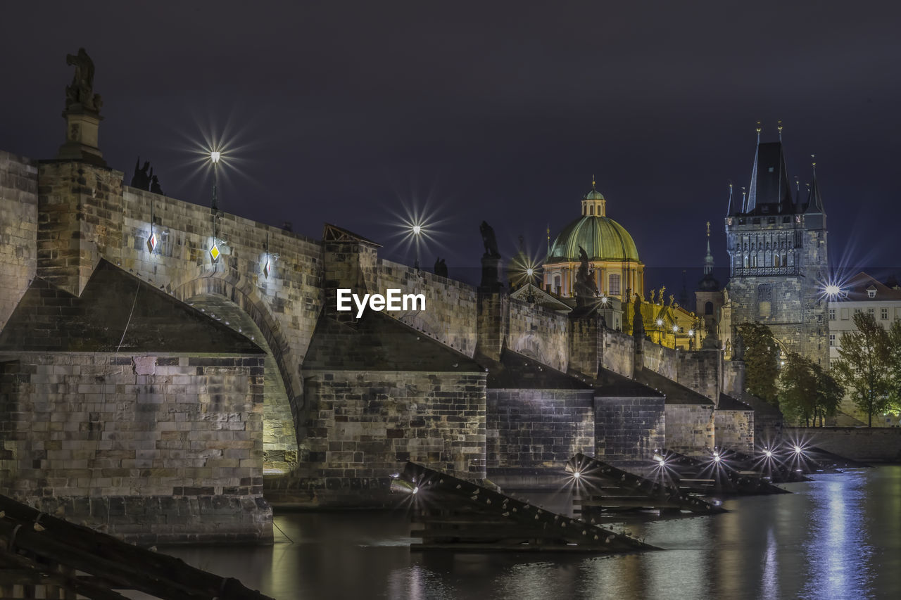 Low angle view of illuminated bridge over river against sky at night