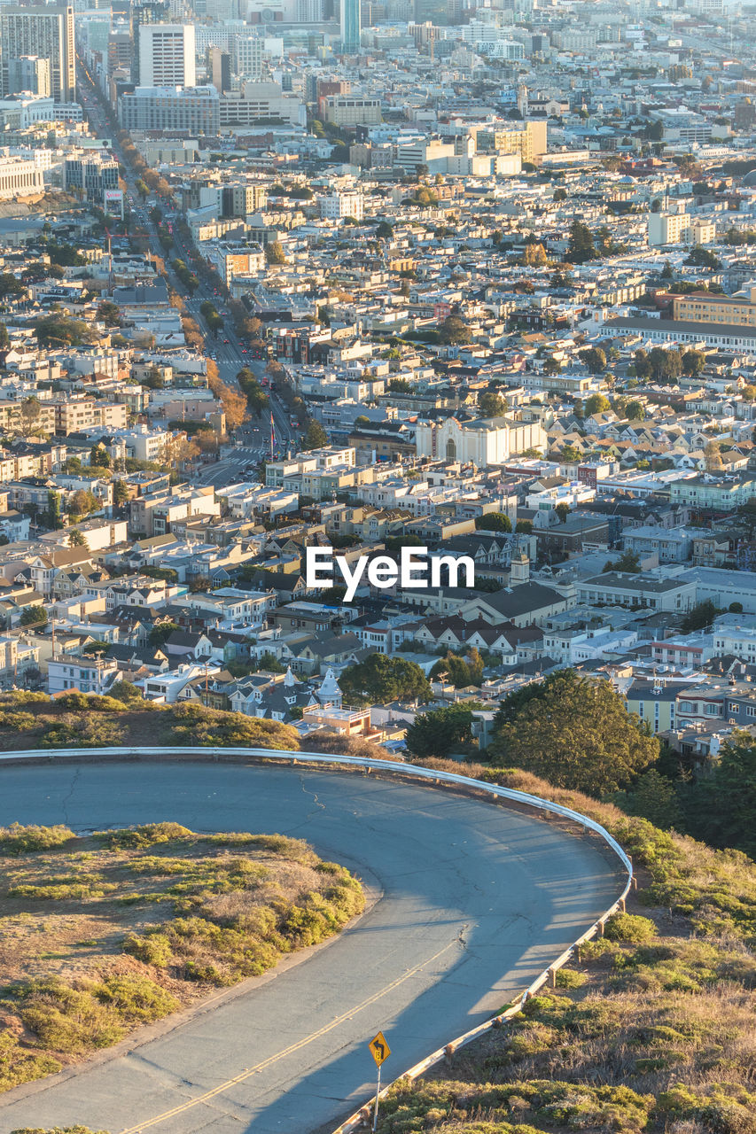 HIGH ANGLE VIEW OF ROAD BY BUILDINGS AGAINST CITY