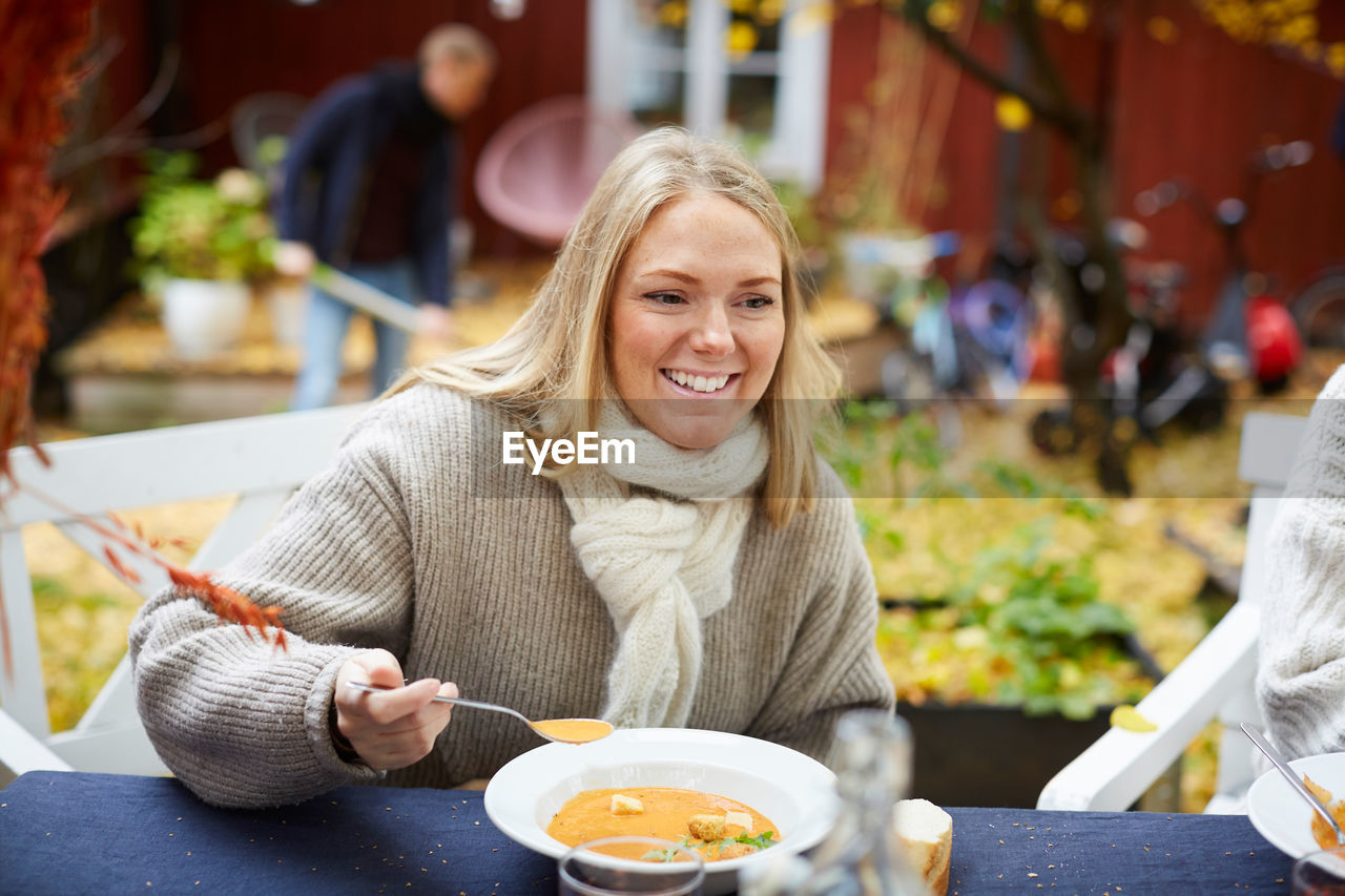 Happy female with vegetarian soup sitting by table at yard