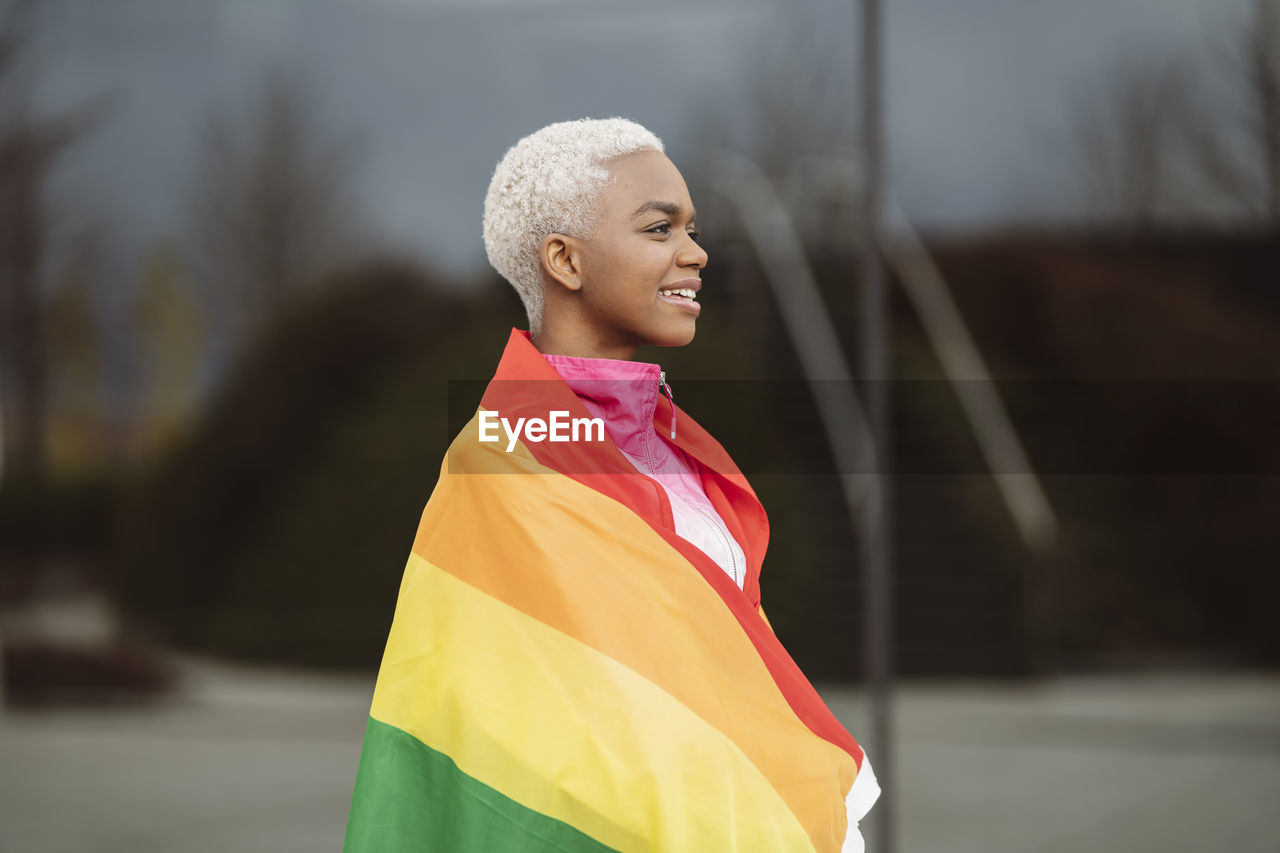 Smiling lgbtqia woman wrapped in rainbow flag