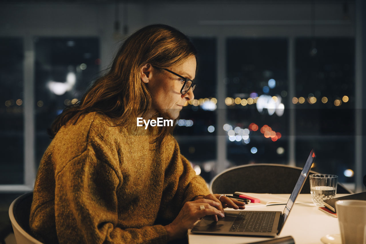 Ambitious businesswoman using laptop while working late at creative office