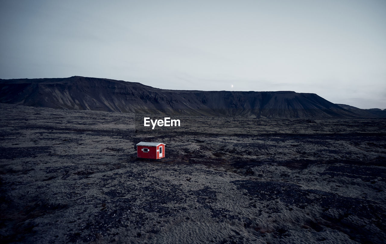 Small red house in dark dry terrain surrounded by hills