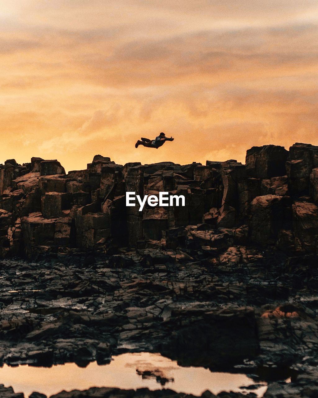 Low angle view of man jumping above rock formations at sunset