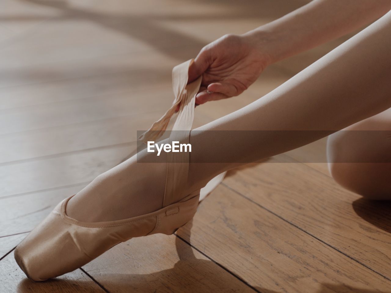 Low section of woman tying shoelace on hardwood floor