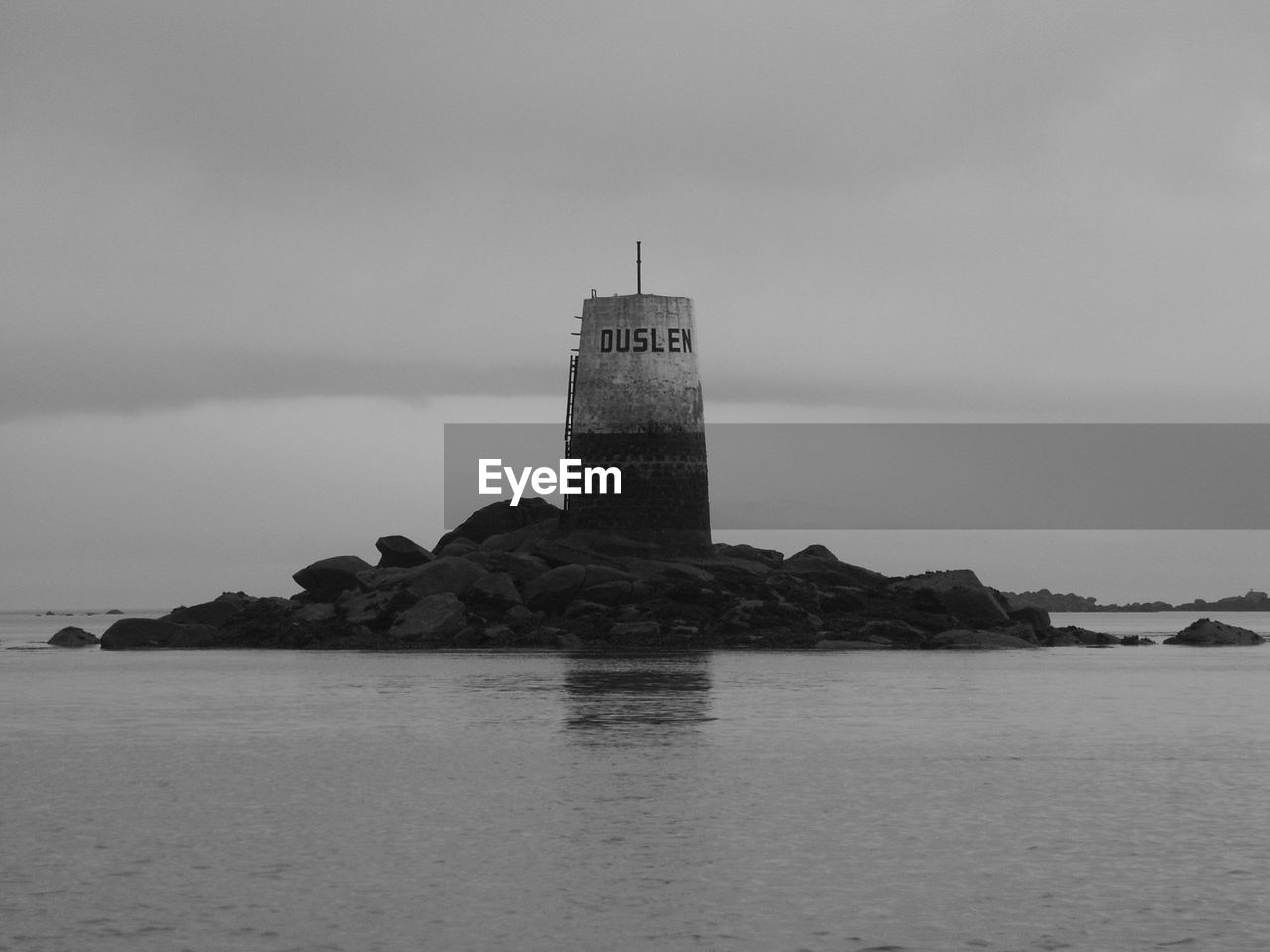 Tower on rocks amidst sea against cloudy sky