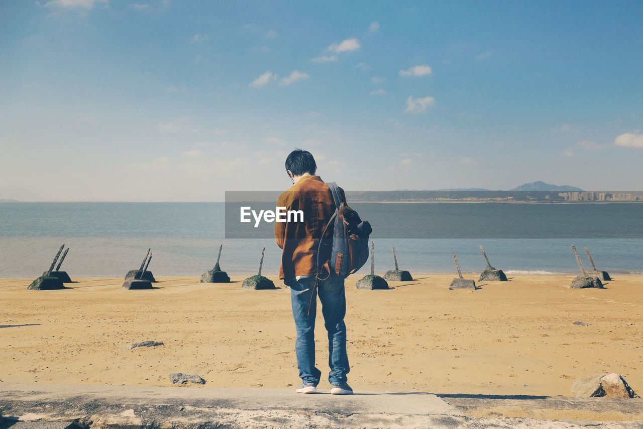 Rear view of man standing at beach against sky