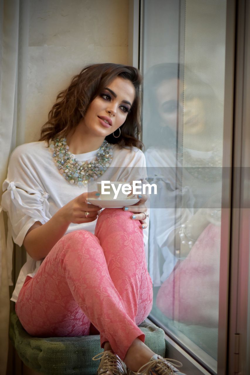 Young woman looking through window at home