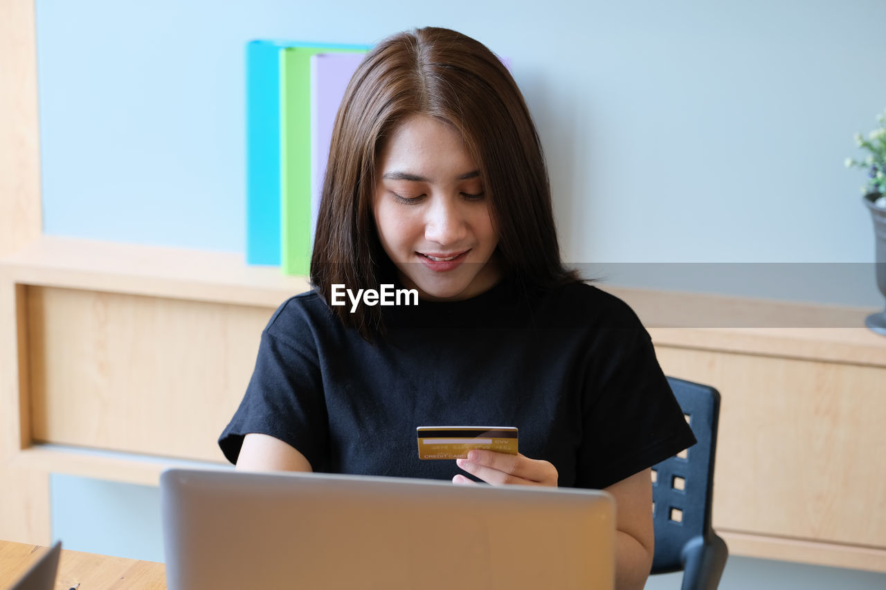 YOUNG WOMAN LOOKING THROUGH SMART PHONE WHILE SITTING ON TABLE