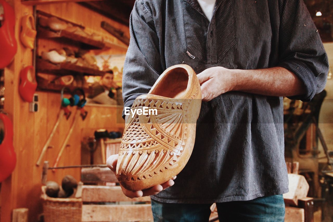 Midsection of man holding wooden shoe in workshop