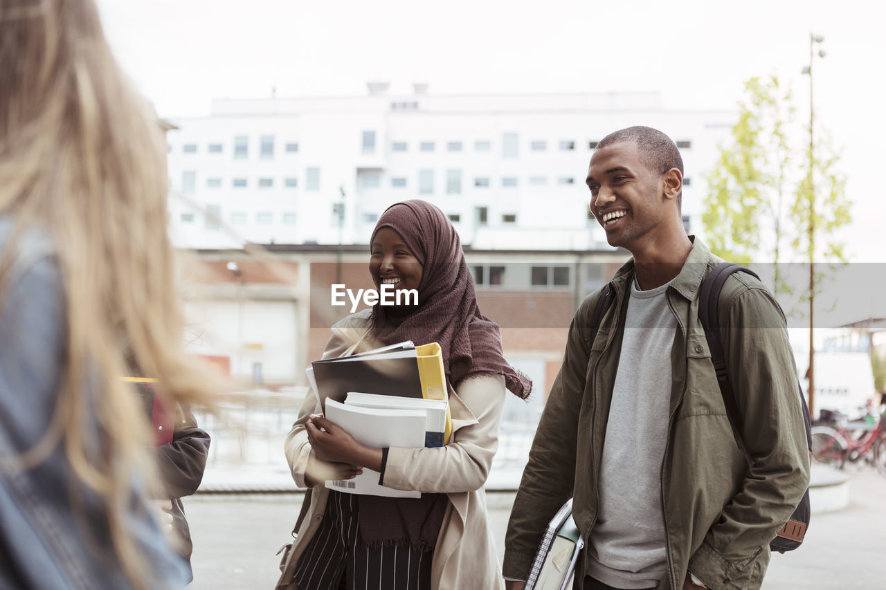 Smiling male and female students standing with friends at university campus