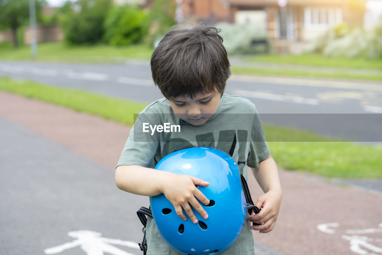 Boy holding blue helmet on road in city