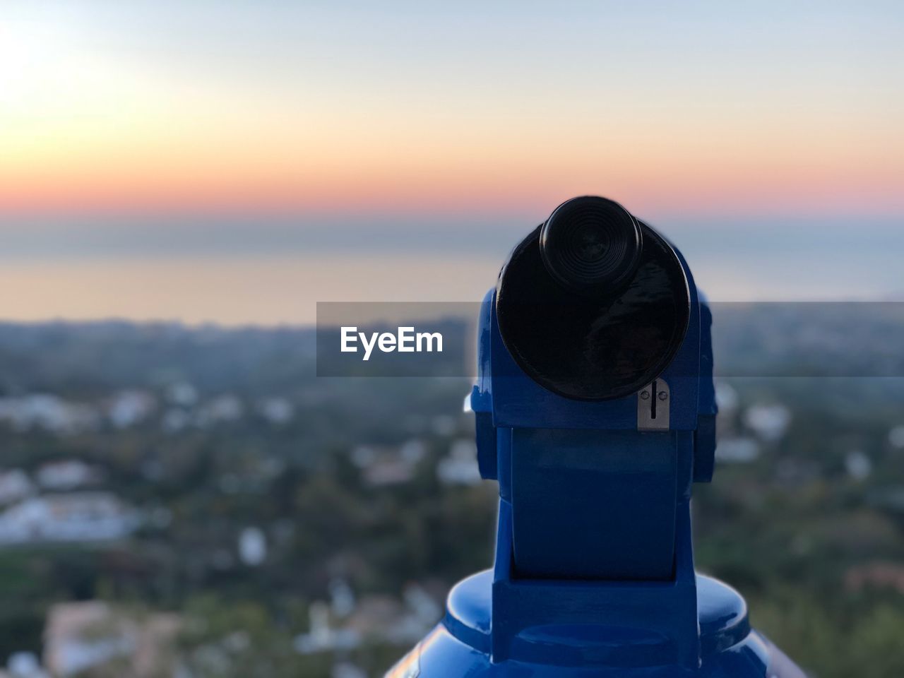 Close-up of coin-operated telescope against cityscape during sunset