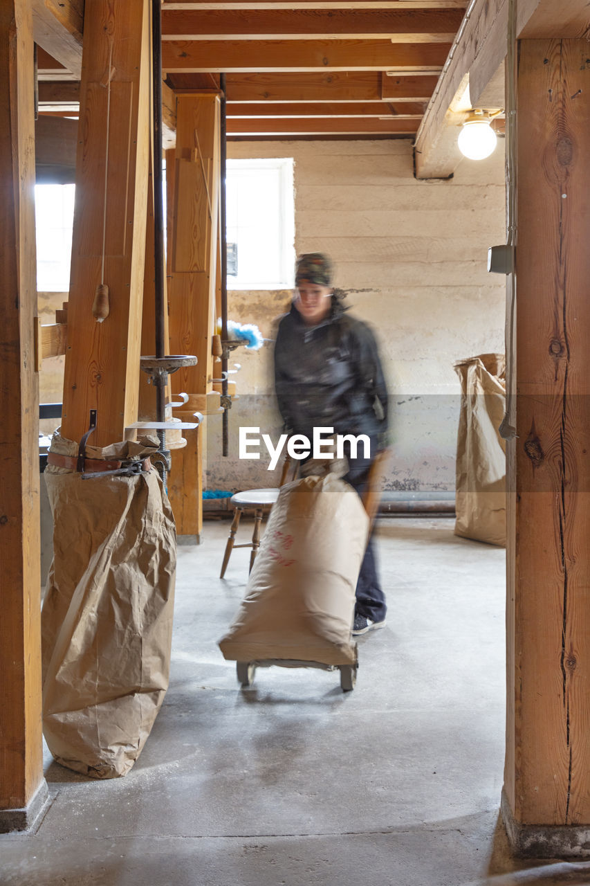 Woman in mill pushing sack on sack barrel