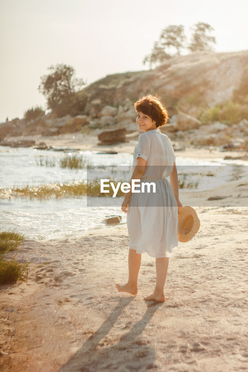 REAR VIEW OF WOMAN STANDING ON LAKE