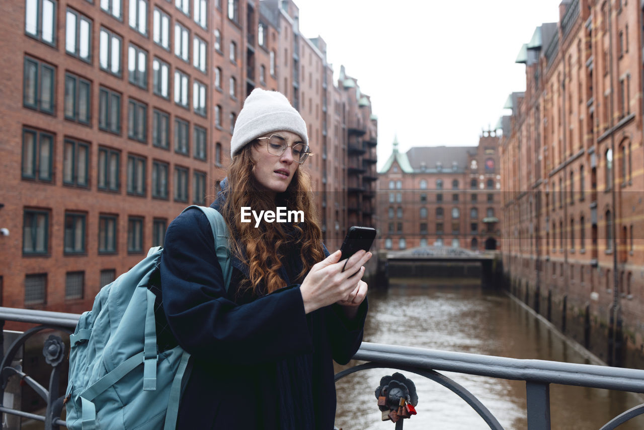 Tourist with backpack using smart phone near buildings in speicherstadt