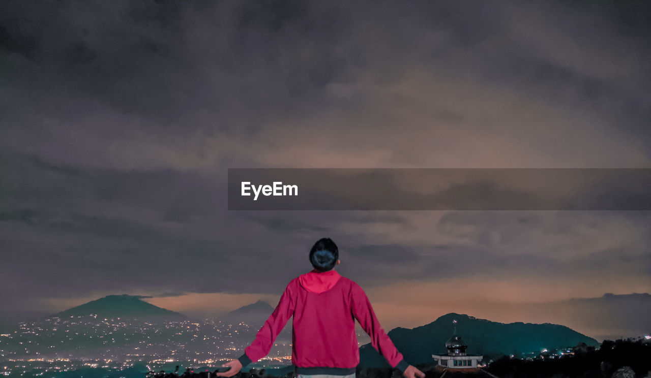 Rear view of woman standing on mountain against sky during sunset