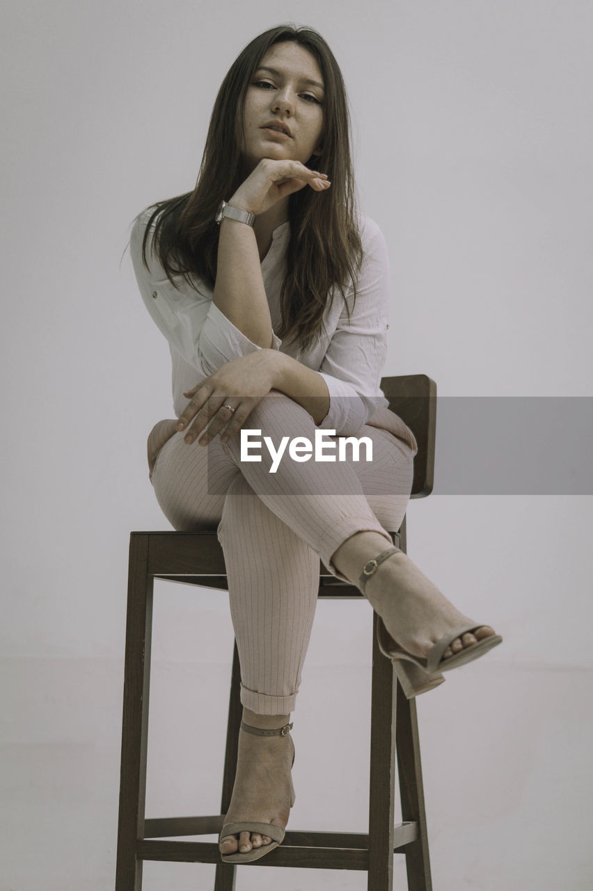 Young woman sitting on chair against wall