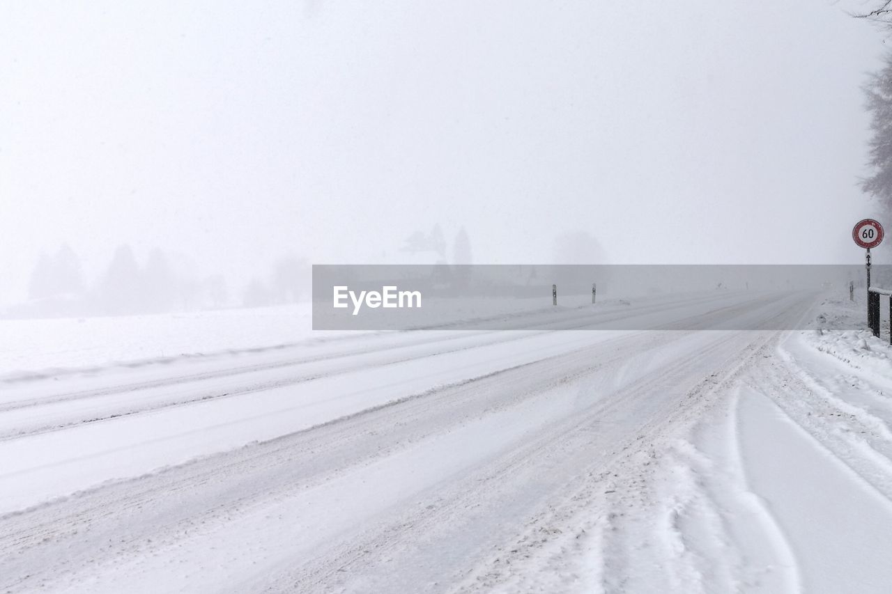 ROAD AMIDST SNOW COVERED LANDSCAPE AGAINST SKY