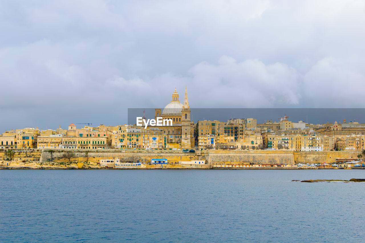 Valletta skyline against cloudy sky with church and buildings in mediterranean sea, malta