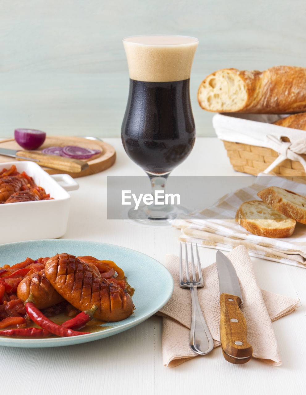 Baked sausages in dark beer with red onion, paprika, red hot chilli, bread and glass of dark beer.