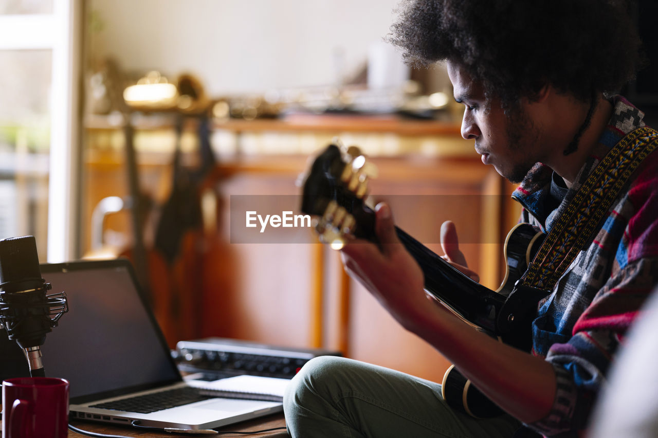 Afro male musician practicing guitar at home