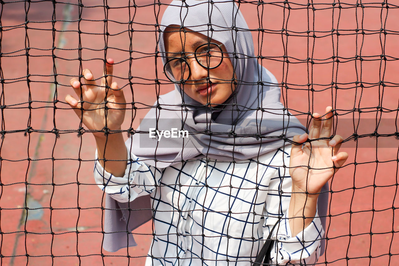 Asian muslim woman, wearing headscarf and glasses taking photo on tennis ball court