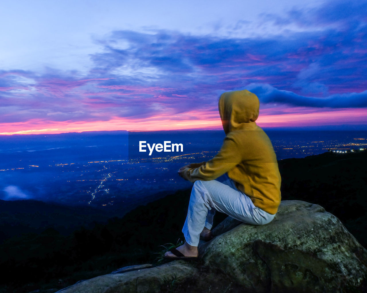 WOMAN SITTING ON ROCK AGAINST MOUNTAIN