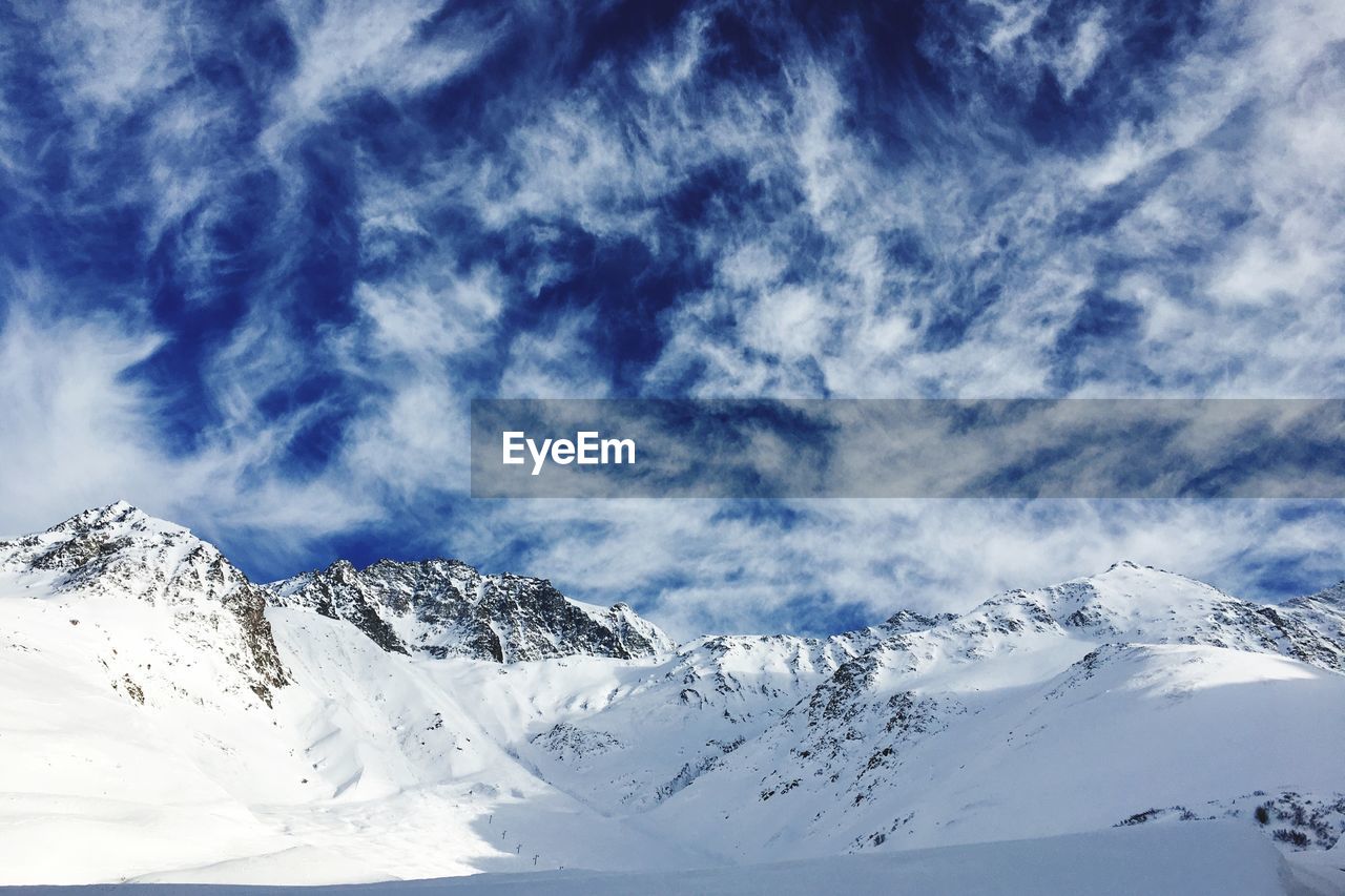 Low angle view of snowcapped mountains against blue sky