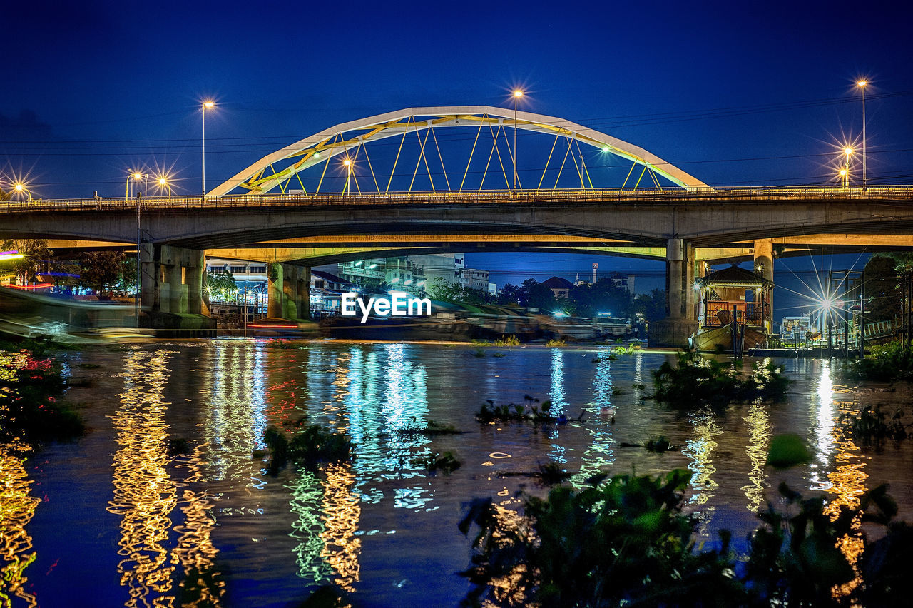 Illuminated bridge over river against sky at night