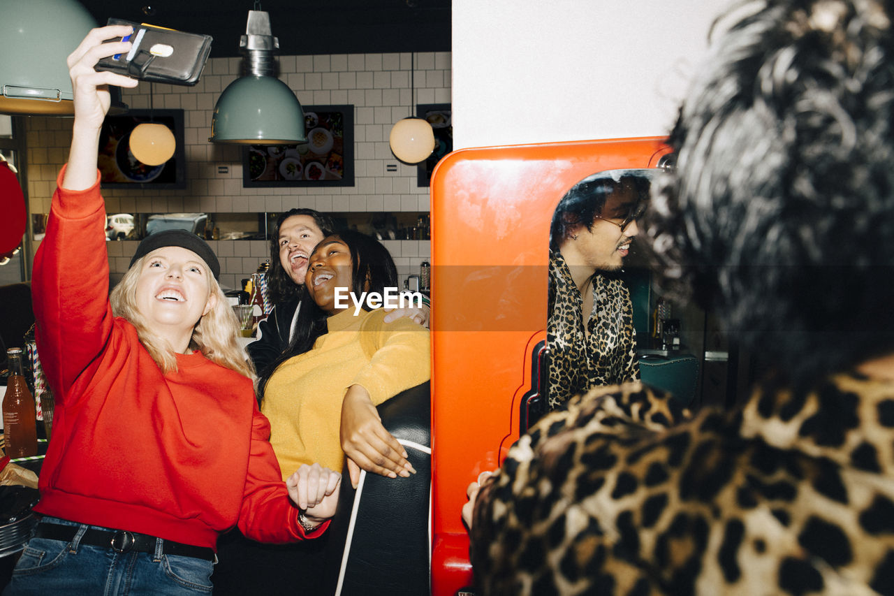 Smiling female taking selfie with friends in cafe