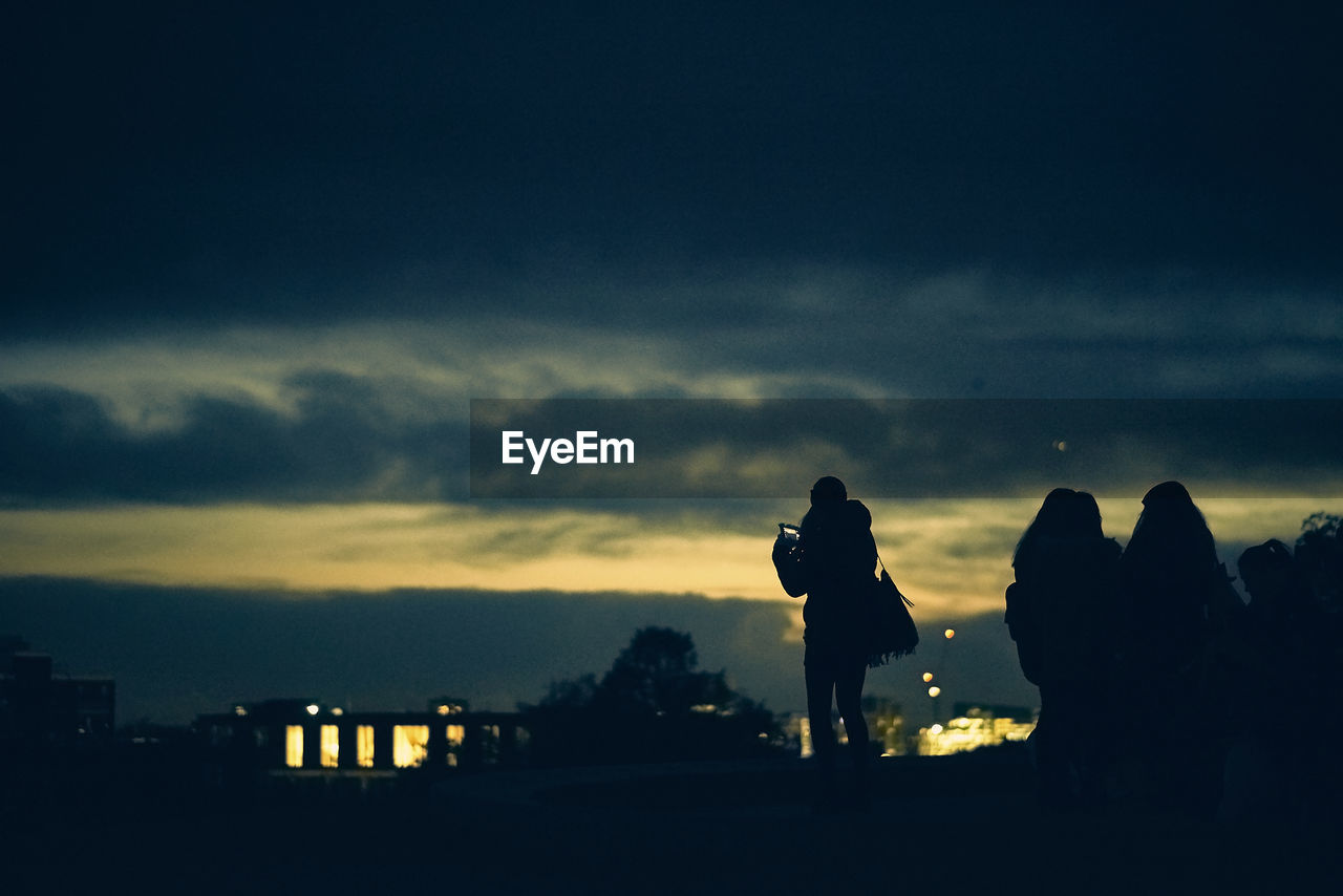 Silhouette people standing against cloudy sky during sunset