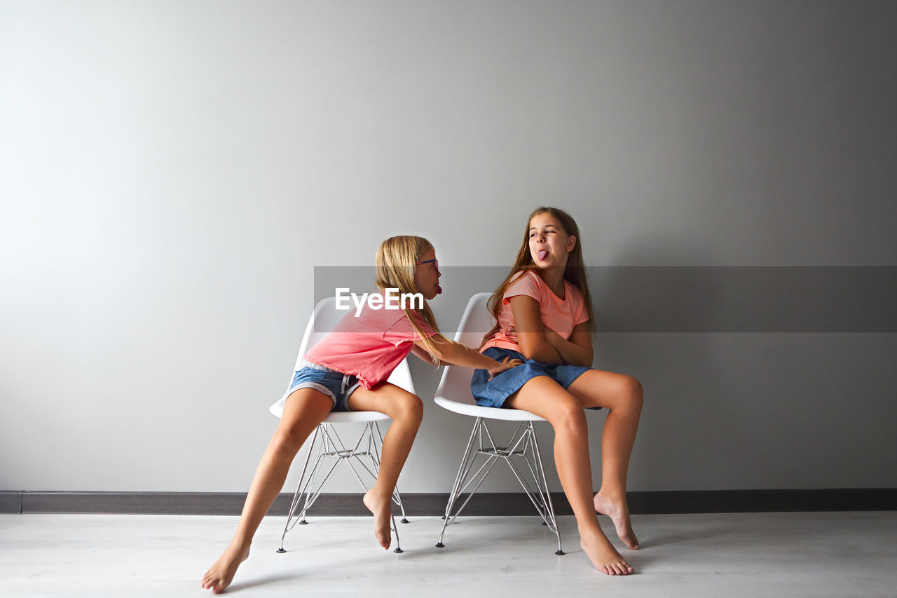 Full length of girls sitting on chairs against wall