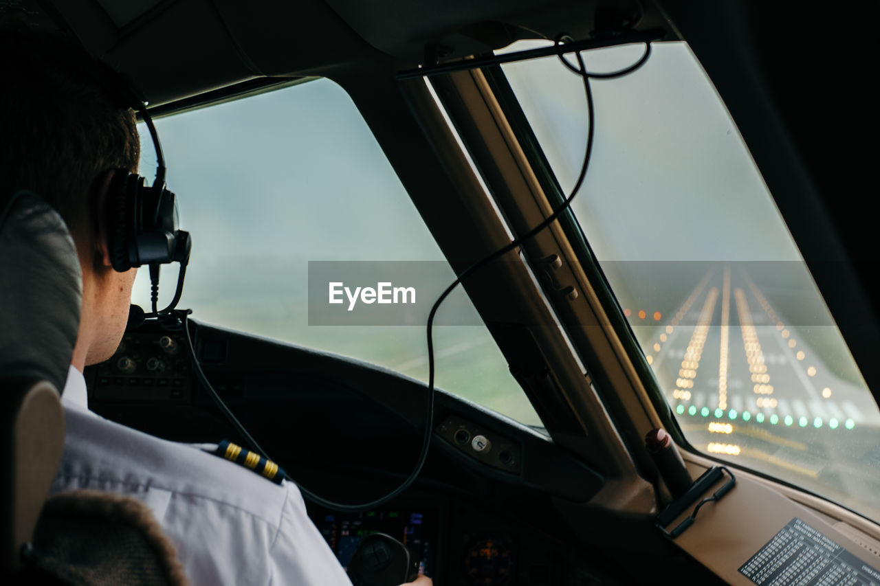 Rear view of man looking through airplane window with pilot