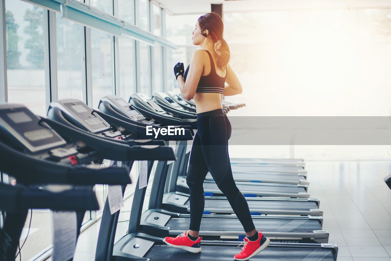 Side view of young woman walking on treadmill at gym