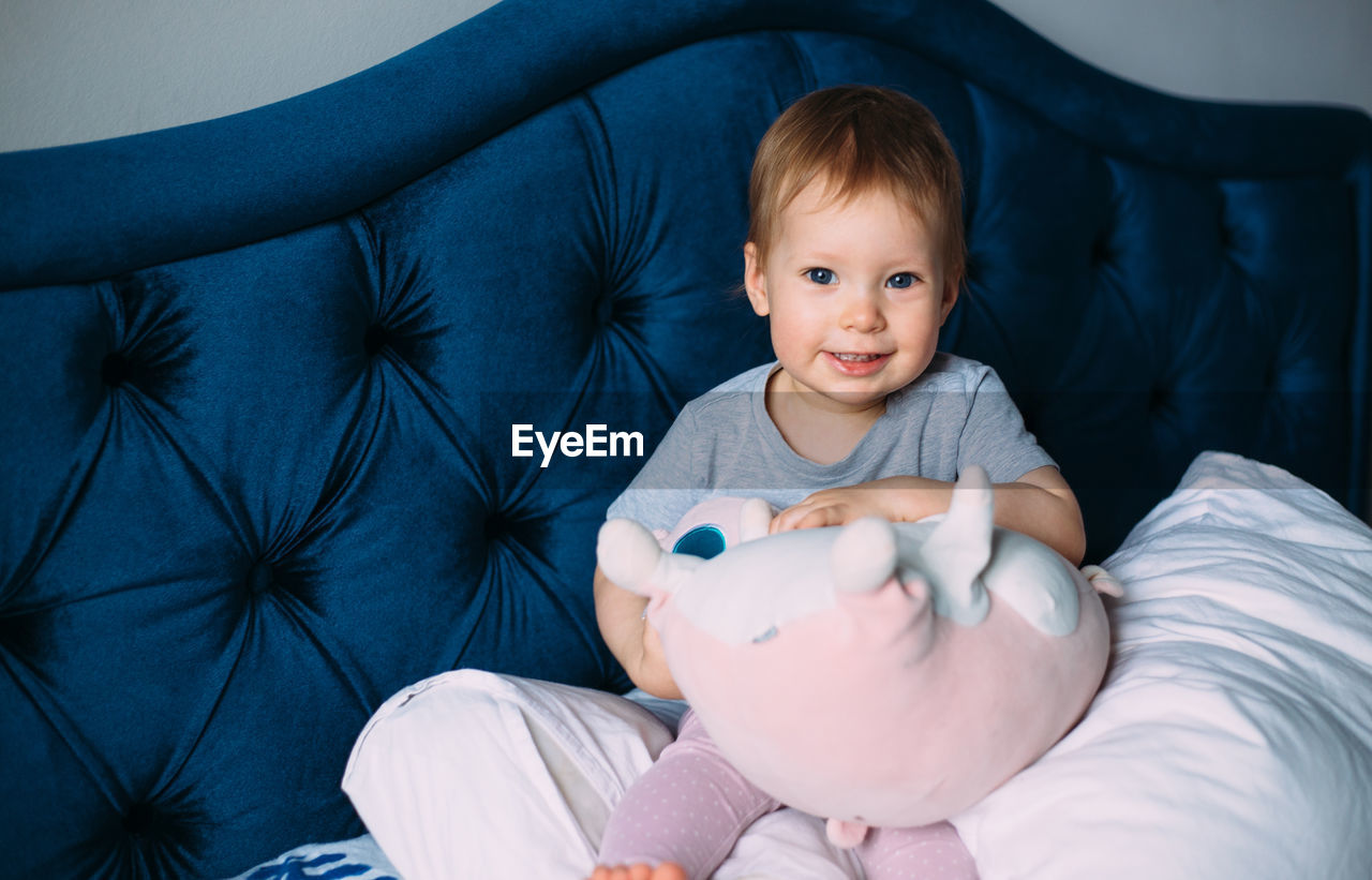 Funny little child is having fun, playing with soft toys on the couch at home.