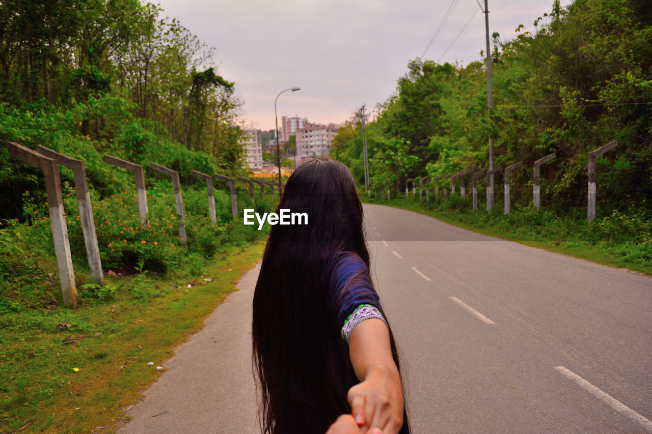 Rear view of woman holding cropped hand on road 