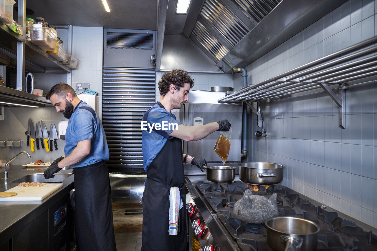 Side view of male chefs preparing food in commercial kitchen